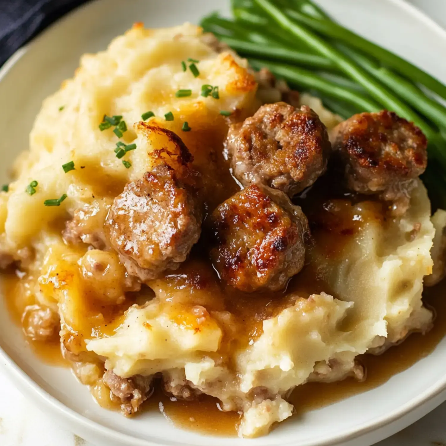 A plate with mashed potatoes, savory sausage gravy, and green beans on the side.