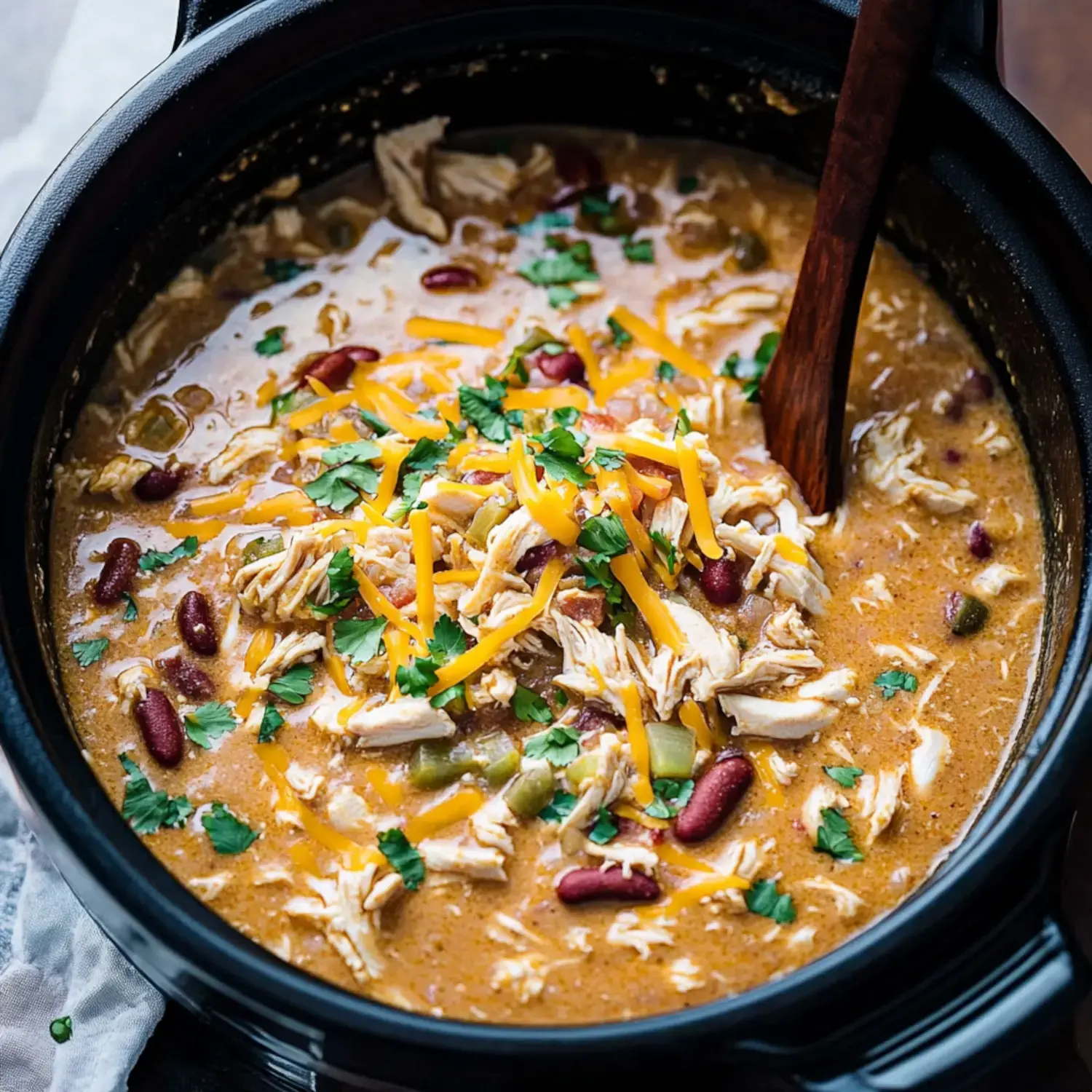 Close-up of creamy chicken chili sprinkled with shredded cheese and herbs.
